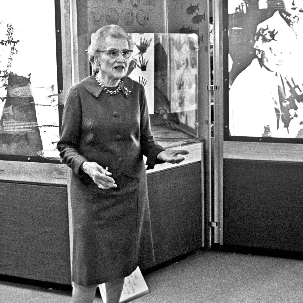 A photograph of Helen Battle in front of a glass case in a museum.