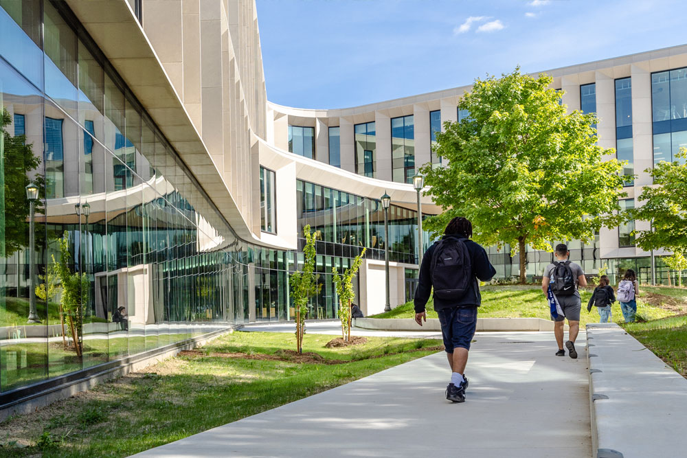 Building exterior with people walking along the adjacent sidewalk during mid-day.