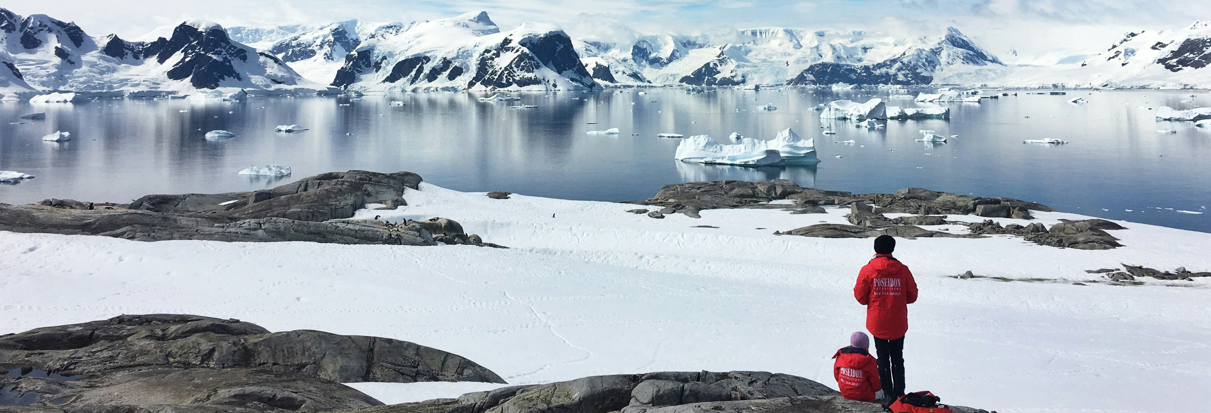 Two individuals in red coats looking out across the water and the ice caps in the Arctic. Decorative image.
