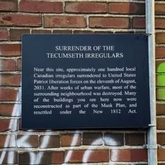 Plaque on graffittied wall with title "surrender of the Tecumseth irregulars"