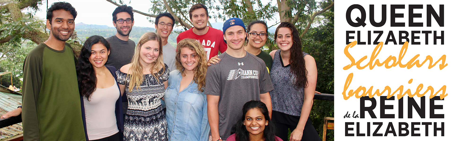 Group of students standing on a hill with dense forest visible in the background. QES logos in both french and english are displayed on the right hand side of the image