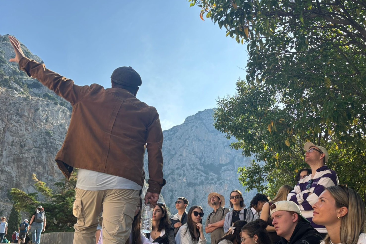 Teacher gestures to landscape in Greece with students looking on