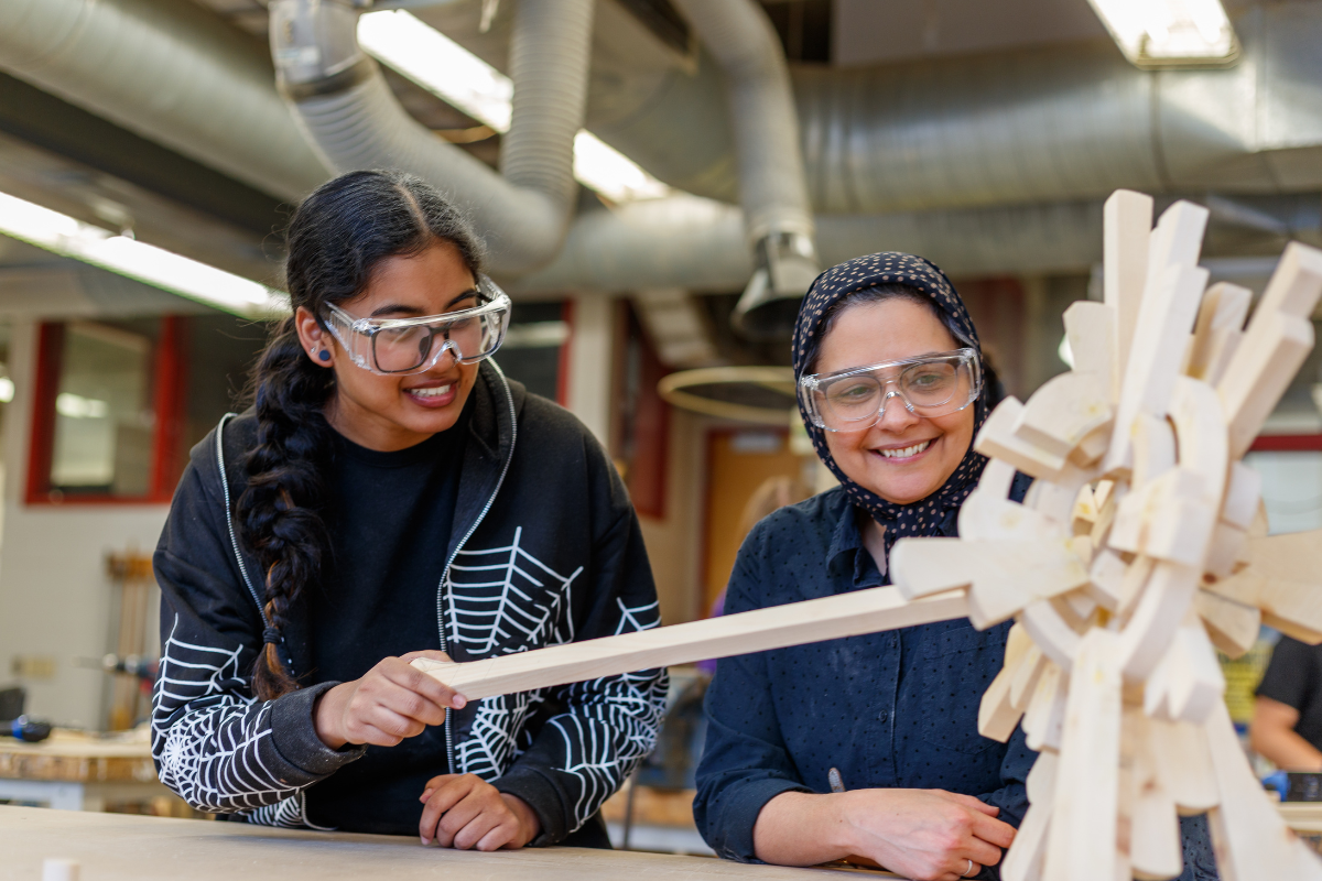 Student and teacher adjusting sculpture, both wearing safety glasses