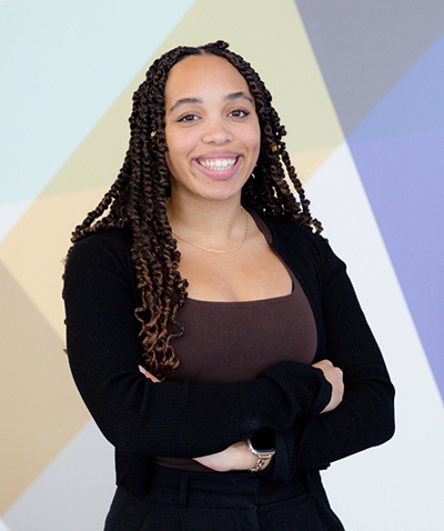 A photograph of a woman standing in front of a colourful background with her arms crossed