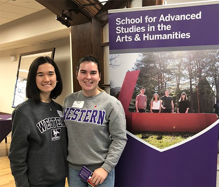 Two students in Western sweatshirts stand in front of a promitional banner for SASAH