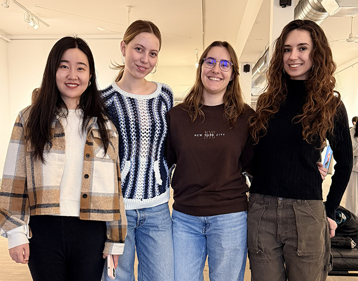 Four students standing together in an art gallery and smiling at the camera