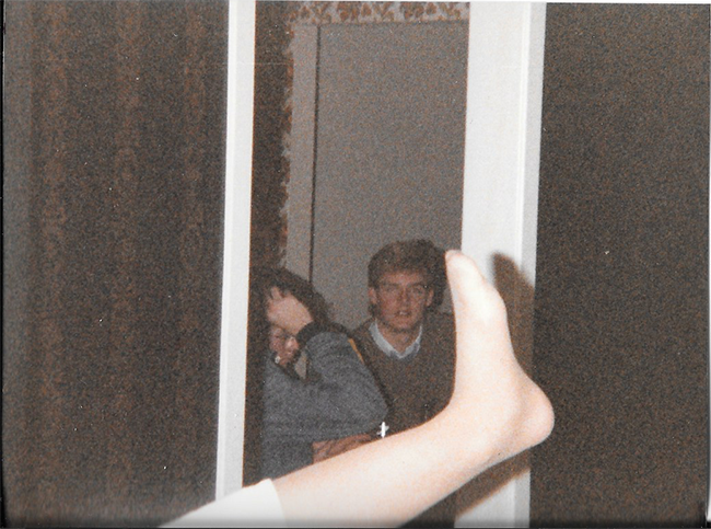 An old colour flash photograph showing a stockinged foot in front of two people