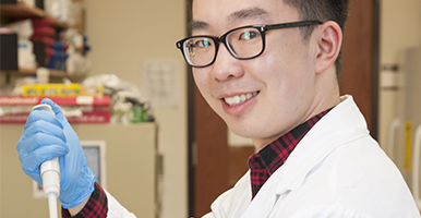 Fourth year student in lab coat looking into camera for Admission Requirement