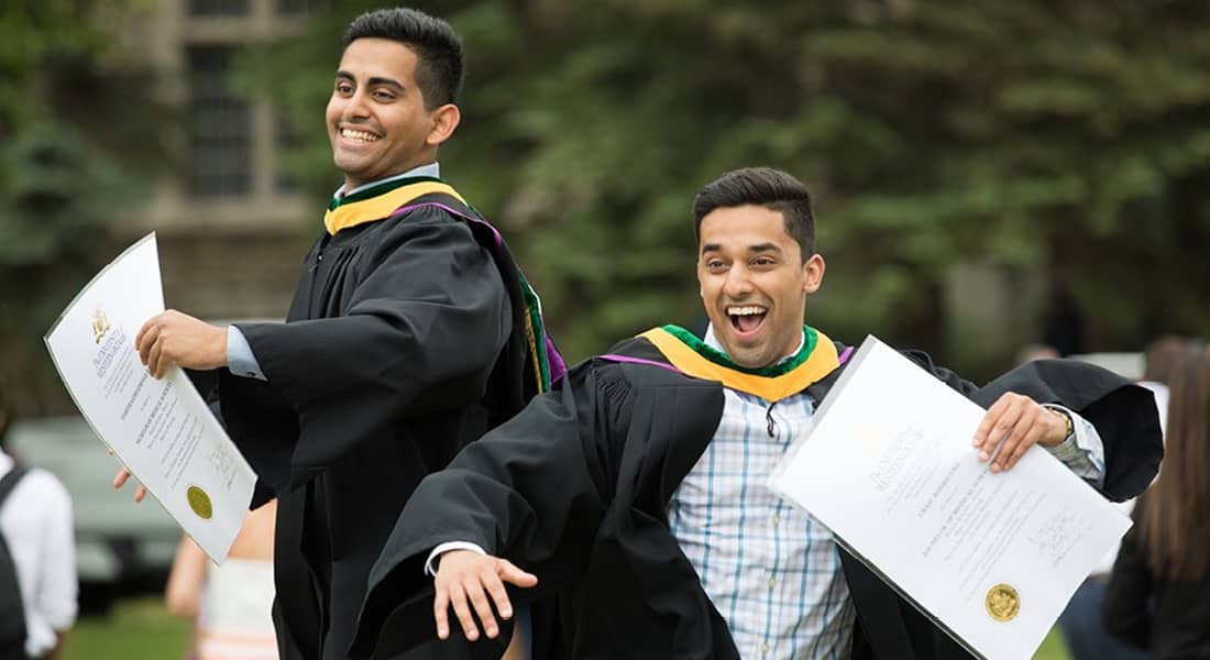 Two men jumping in the air holding their diplomas