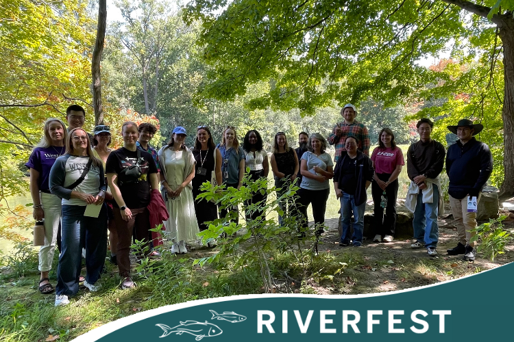 Group of people standing outside in a forested area by the river