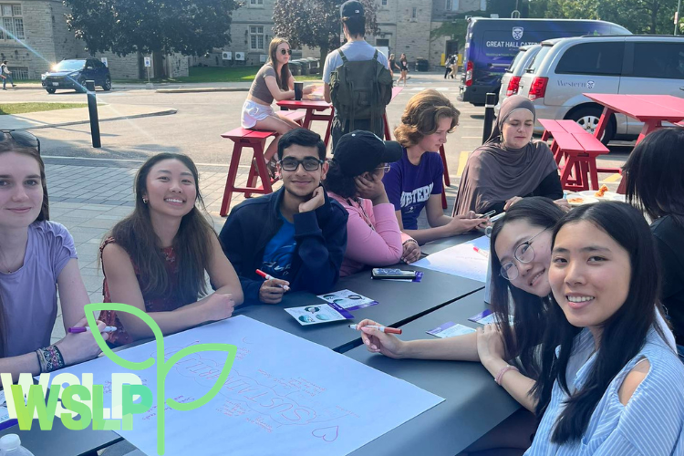 Group of students sitting outside at a table writing on chart paper