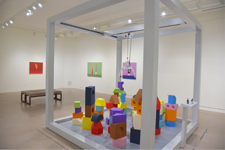 An art installation featuring a large claw-crane game, and corresponding paintings featuring similar shapes.