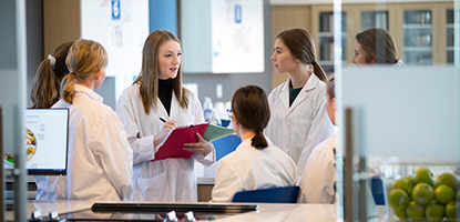 Students in lab coats standing in a circle discussing