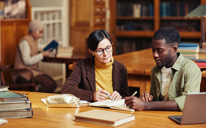 A professor and a student sitting at a desk reviewing notes.