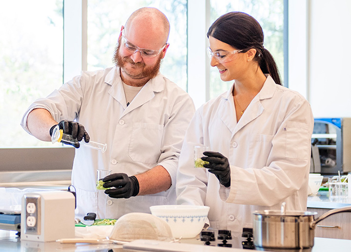 Two students wearing lab coats conducting research in a food lab.