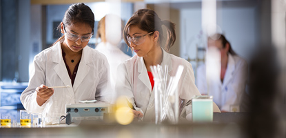 Two students wearing lab coat researching in food lab