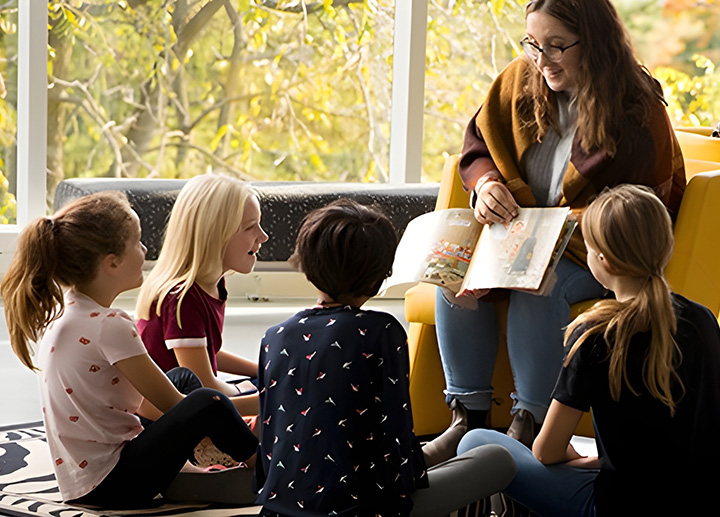 Undergraduate student reading to children sitting around her.