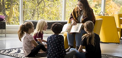 Undergraduate student reads a book to a group of children