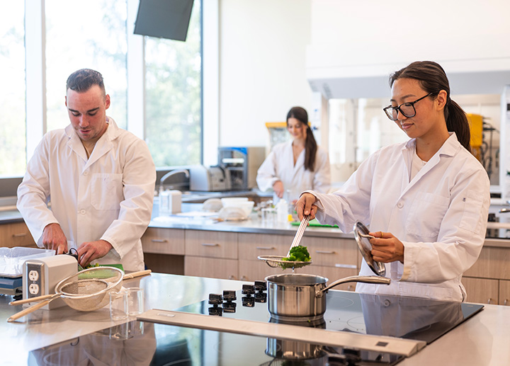 A student lifting a sieve containing broccoli out of a pot.
