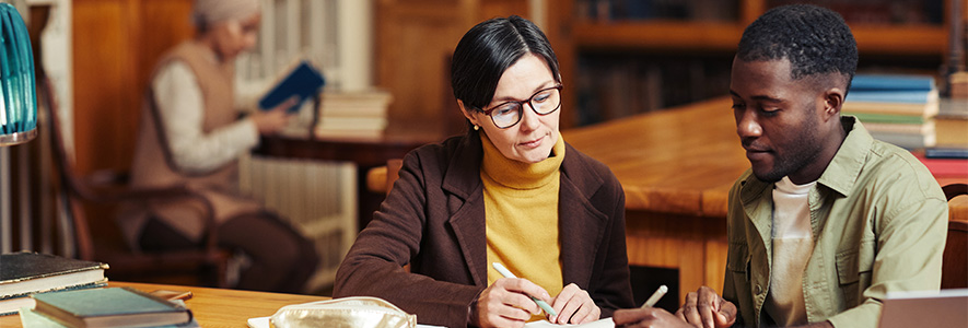 A professor and a student sitting at a desk reviewing notes.