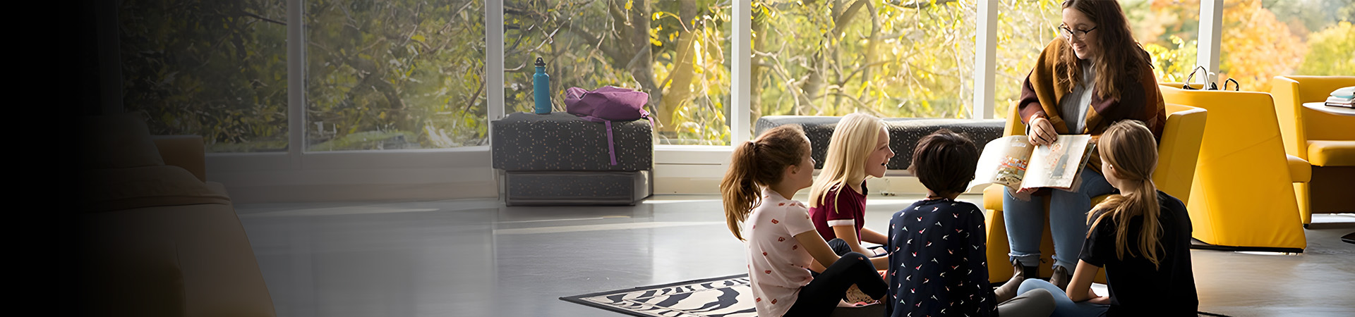 Undergraduate student reading to children sitting around her.
