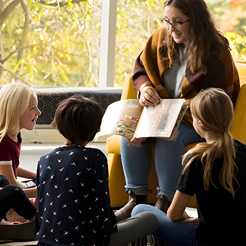 Undergraduate student reading to children sitting around her.