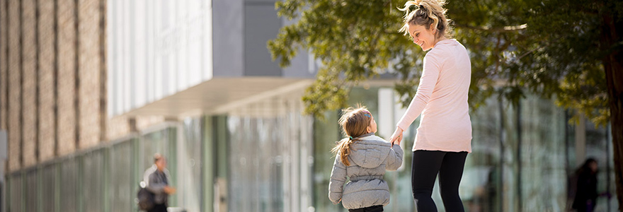 A woman and child walk outside a building holdeing hands on a sunny day. 