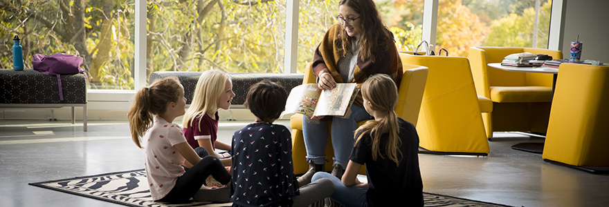 Undergraduate student reading to children sitting around her.