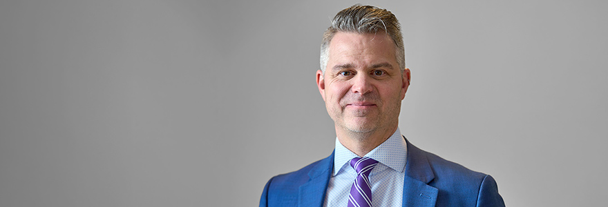 Shaun Boe headshot with blue suit and purple tie.