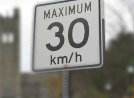 Close up of a roadside which reads; 'Maximum 30 km/h'. The University Tower is blurred in the background.