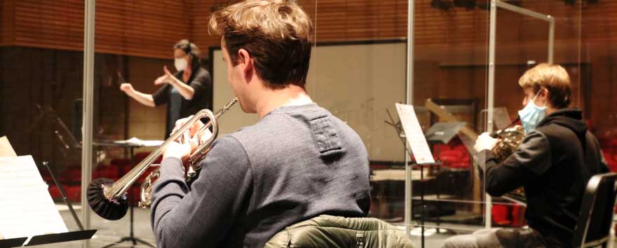 Two students play their instruments behind protective barriers