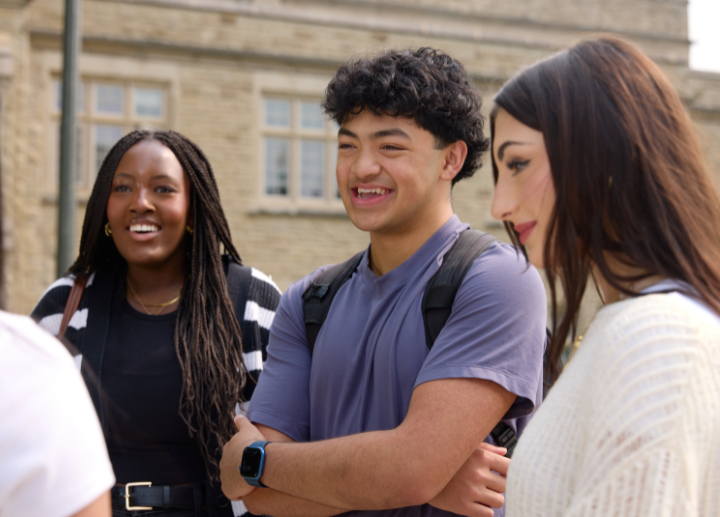 three students standing in a circle, chatting and smiling.