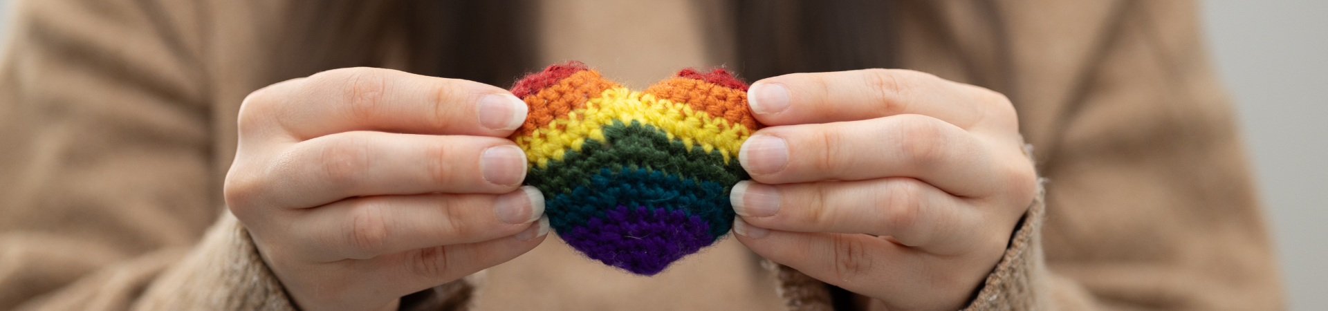 A young woman holds a crochet rainbow heart.