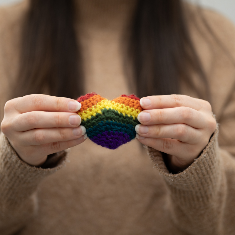 A young woman holds a crochet rainbow heart.