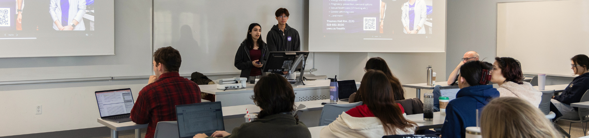 Two students speak to a class of students.