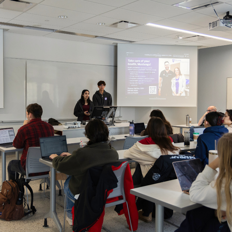 Two students speak to a class of students.