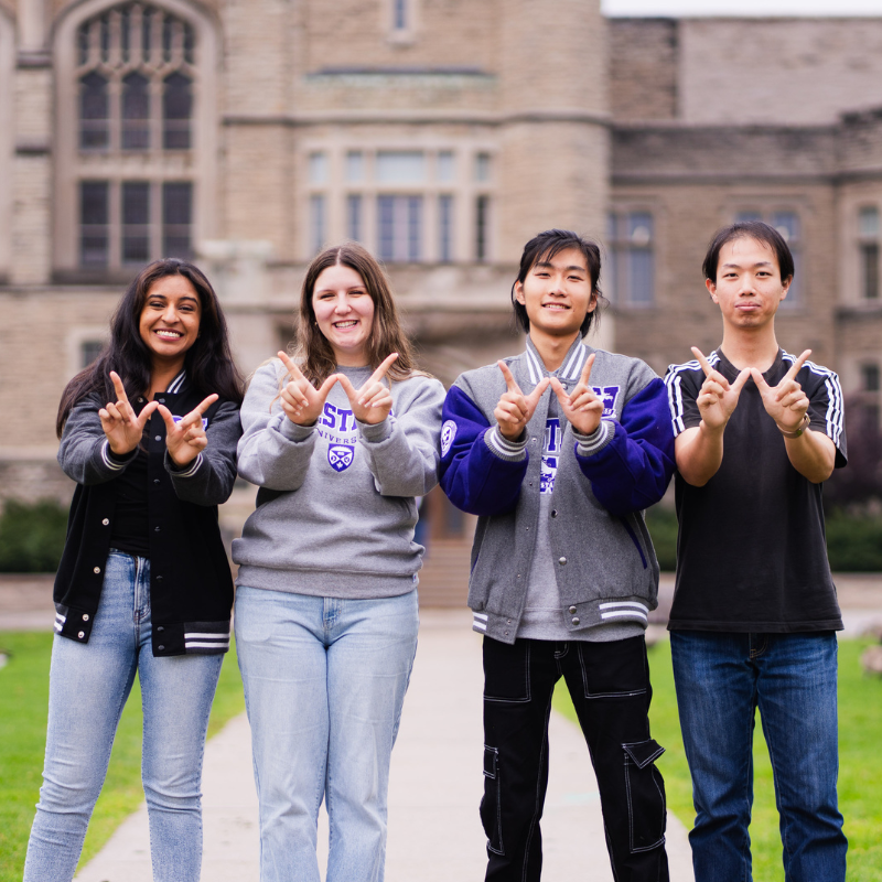Four students holding their hands in the shape of a W for Western.