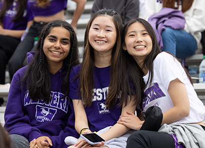 Group of 3 female students hugging each other and wearing Western clothing at a football game