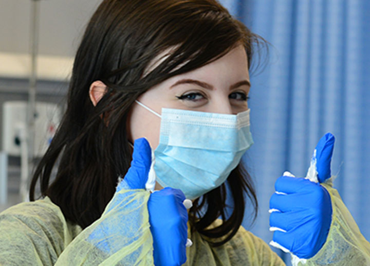 A little girls wearing a mask and latex gloves giving two thumbs up