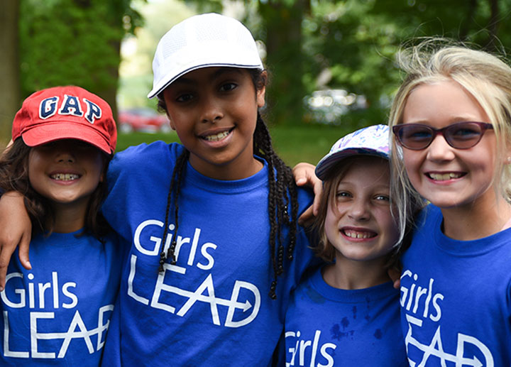 4 little girls hugging each other wearing blue Girls Lead shirts