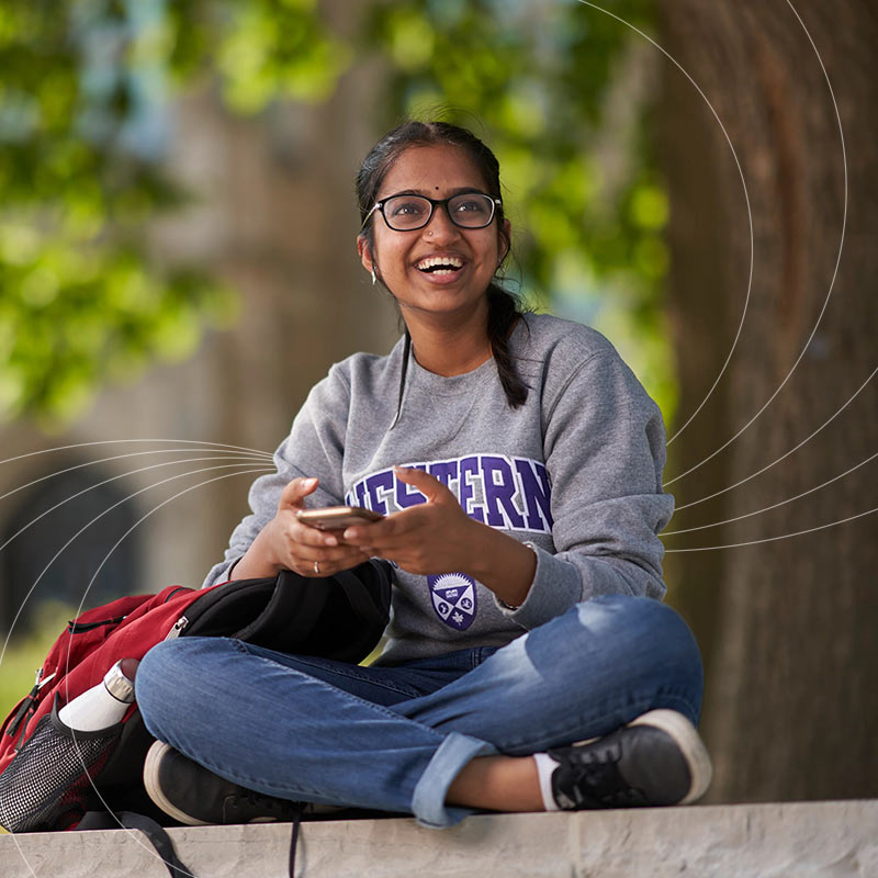 girl sitting cross legged holding her phone and looking up in a surprising smile