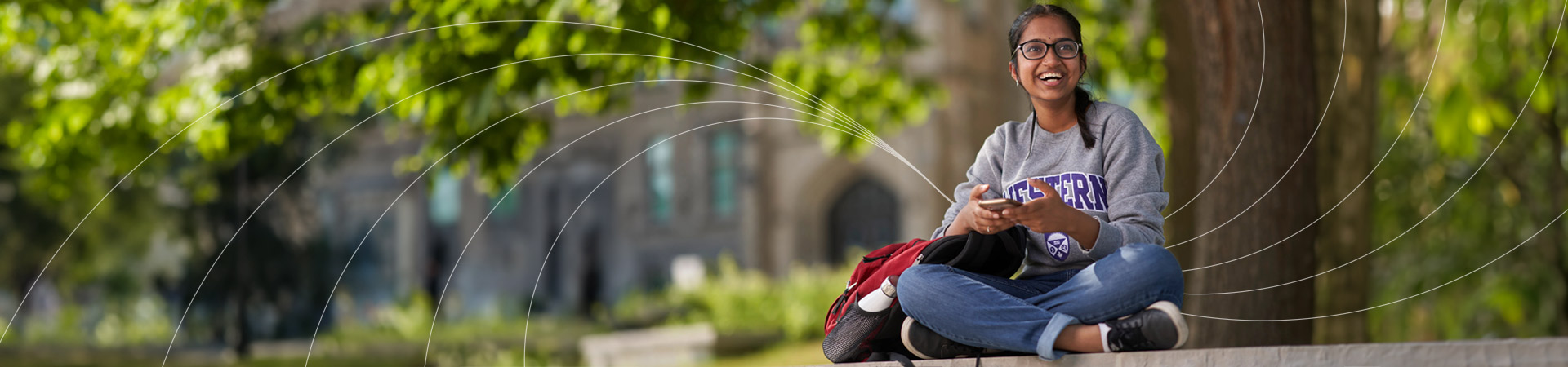 girl sitting cross legged holding her phone and looking up in a surprising smile