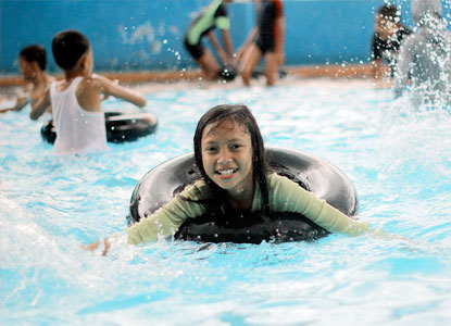 Young girl on an innertube splashing in a swimming pool.