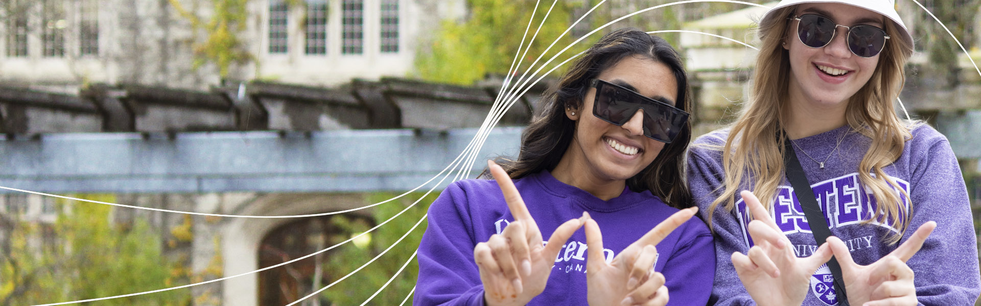 Students smiling holding up a W with white wavy lines across the image