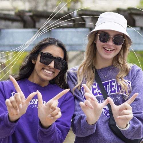 Students smiling holding up a W with white wavy lines across the image
