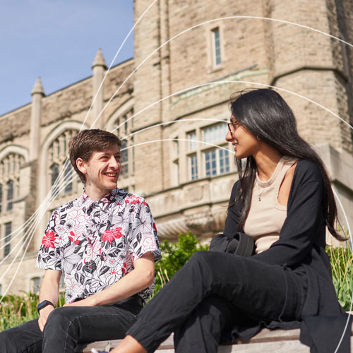 Two students sitting on campus looking to each other smiling. White wavy lines across the photo.