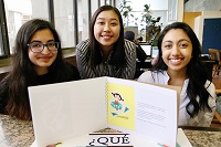 Three female introductory Spanish students pose smiling with their children's book creation.