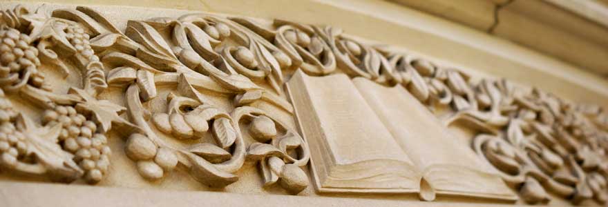 Image of a stone facing of a building that consists of a book and foliage.