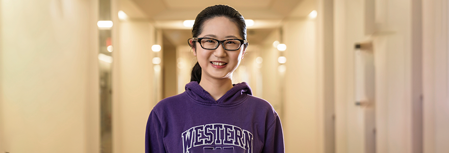 Tianyi stands in a hallway wearing a Western sweatshirt.