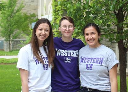 Three students wearing Western clothes smile at the camera